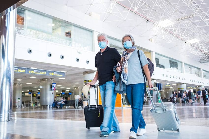 Testpflicht für Flugrückkehrer schon ab Freitag, im Bild : zwei Senioren, die im Flughafen zu ihrem Gate gehen und ihren Flug antreten und dabei eine medizinische Maske tragen