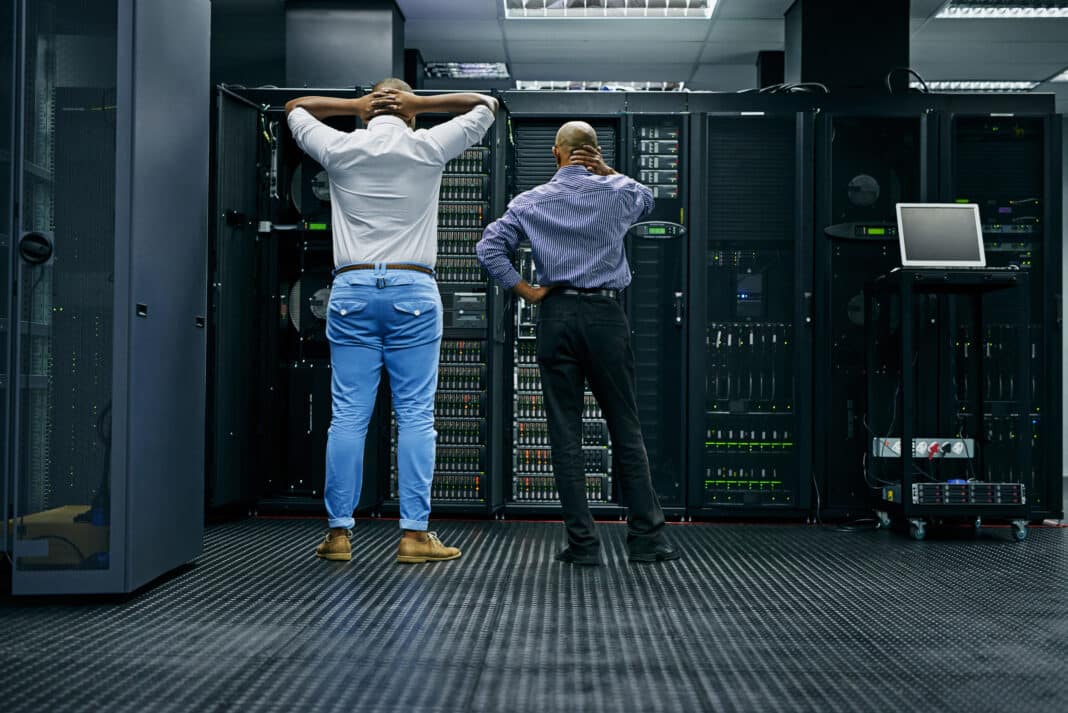 Währenddessen im Serverraum.... Rückansicht von zwei IT-Technikern, die Schwierigkeiten haben, einen Computer in einem Rechenzentrum zu reparieren. Foto: Camerene Pendl /peopleimages.com /Adobe Stock